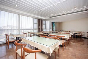 Un comedor amplio con varias mesas y sillas, ventanas grandes y un techo alto.