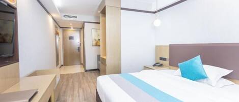 Una habitación de hotel con cama, mesita de noche y escritorio con una computadora portátil.