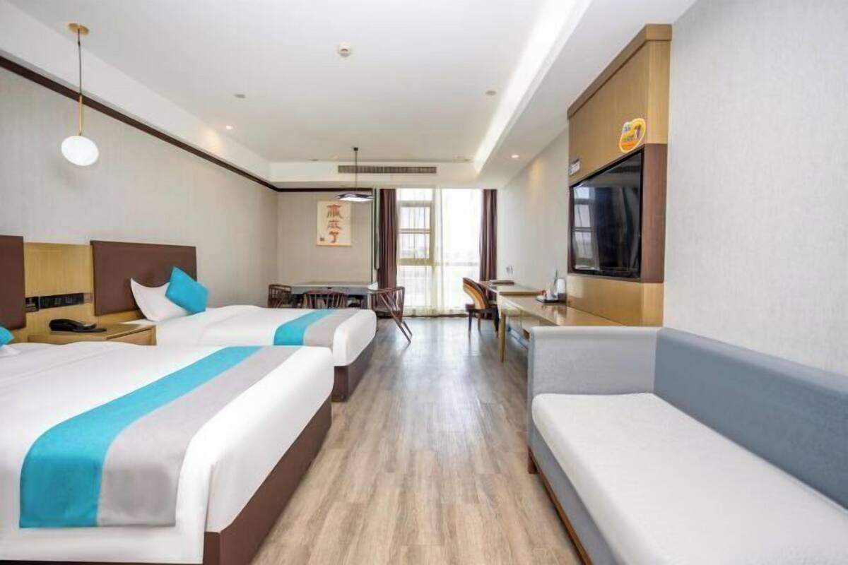 A hotel room with two beds, a desk, a TV, and a sofa.