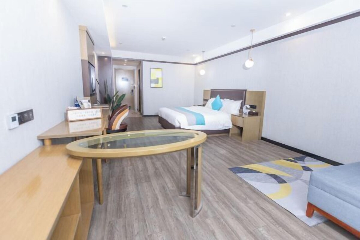 Una camera d'albergo con un letto, un comodino, un tavolino con piano in vetro, un divano e una piccola scrivania con sedia.