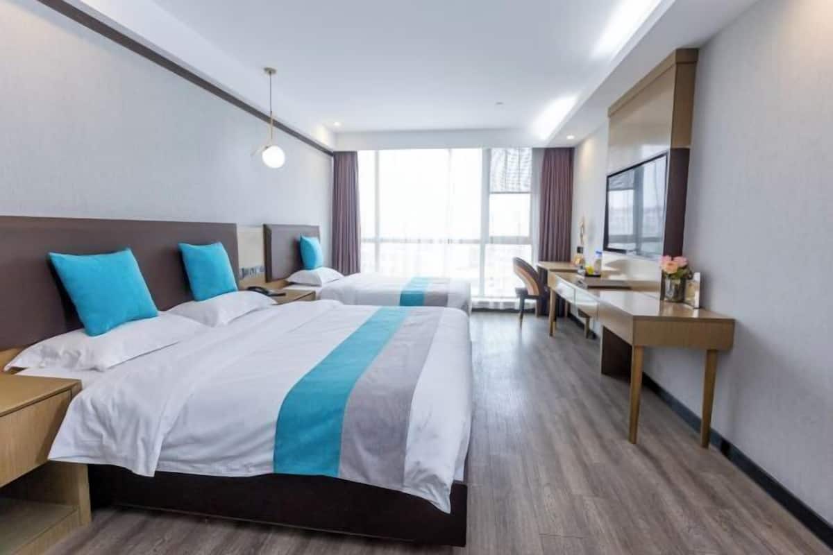 A hotel room with two beds, a desk, and a large window.