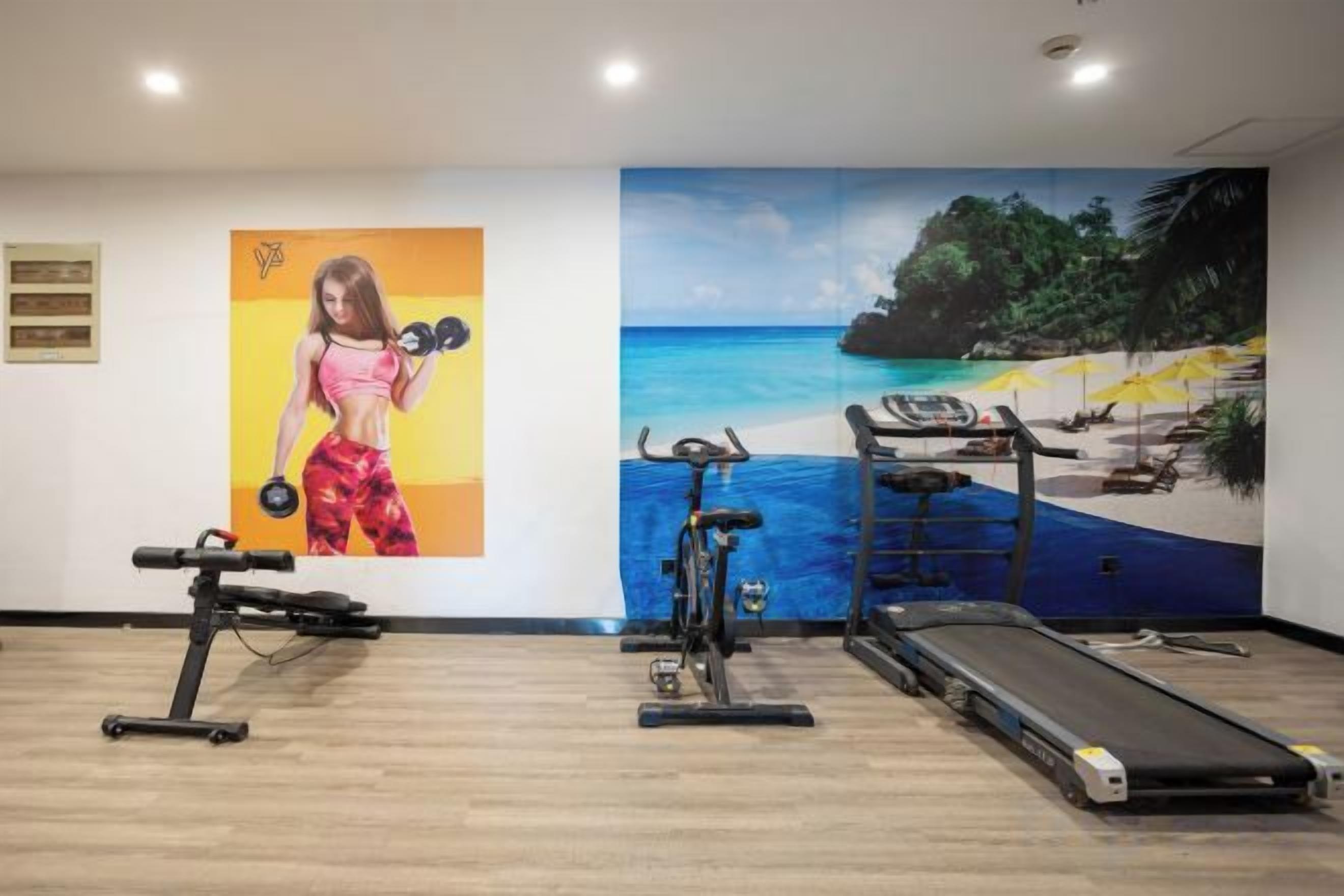 Une salle de sport équipée de matériel d’exercice et ornée d’une fresque représentant une scène de plage.
