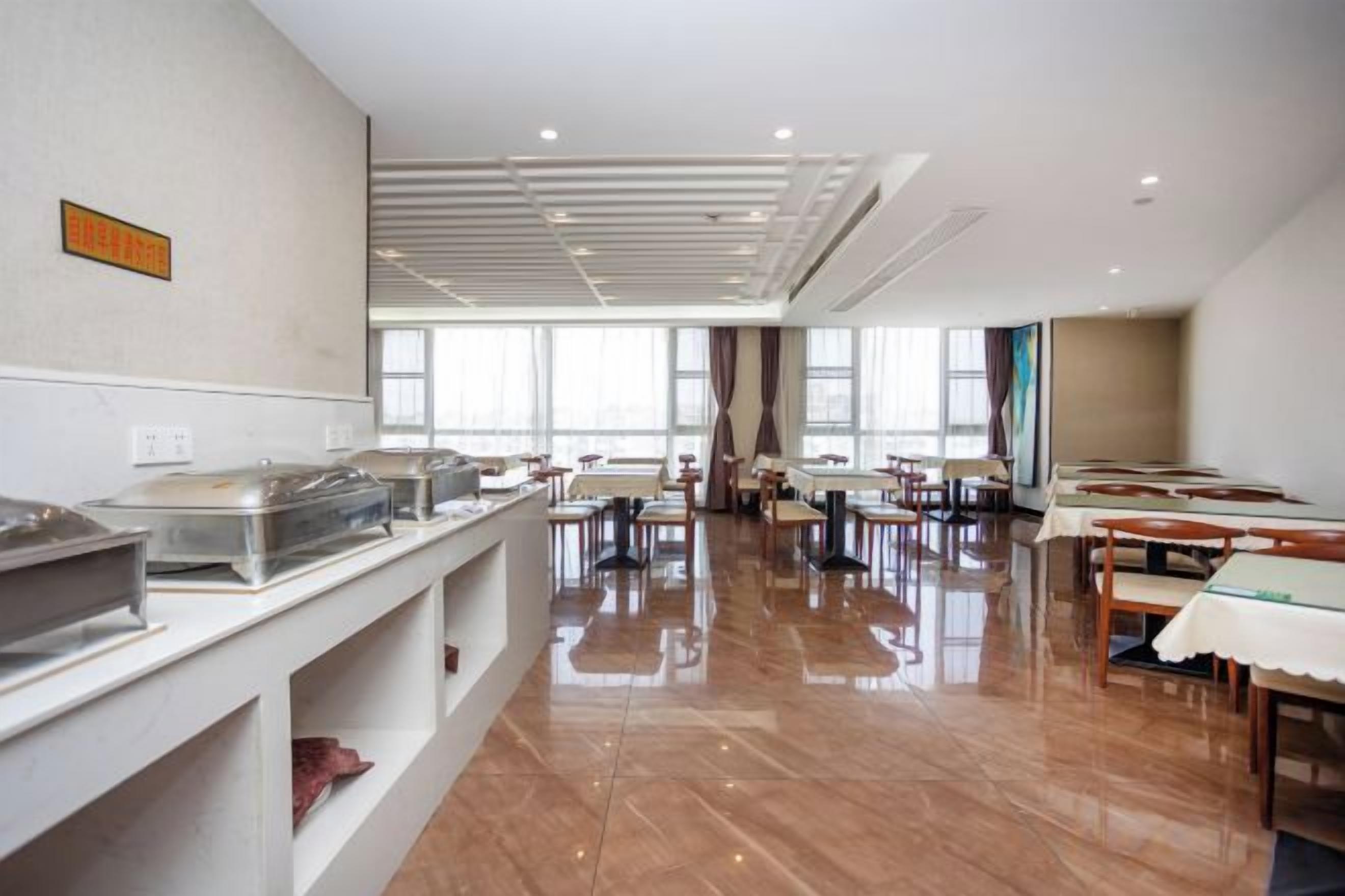 Un comedor amplio con mesas y sillas, una barra de buffet con recipientes de comida, y ventanas grandes que dejan entrar luz natural.