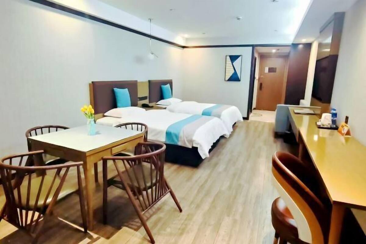 A hotel room with two beds, a dining table with chairs, and a small desk with a chair.