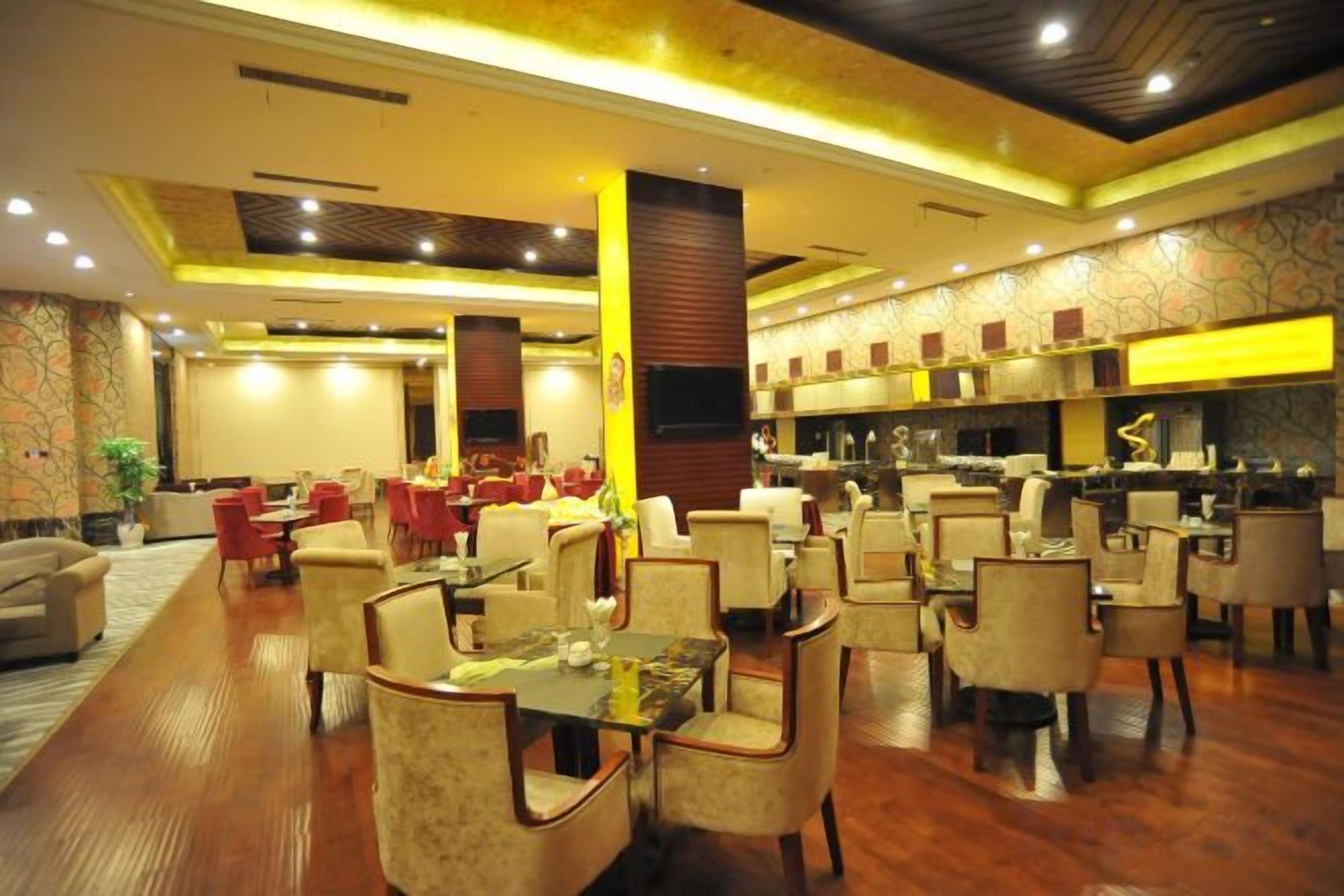 Une salle à manger d’hôtel spacieuse, avec de nombreuses tables et chaises, un pilier central et une cuisine en arrière-plan.