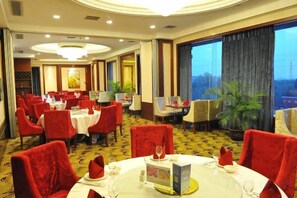 Een restaurant in een hotel met ronde tafels, rode stoelen en uitzicht op de stad.