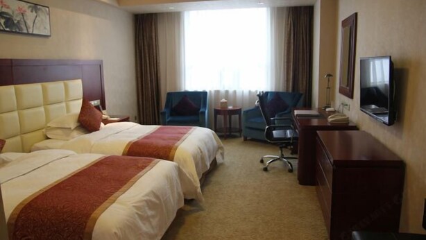 Une chambre d’hôtel avec deux lits, un bureau, une chaise, une télévision et une fenêtre avec des rideaux.