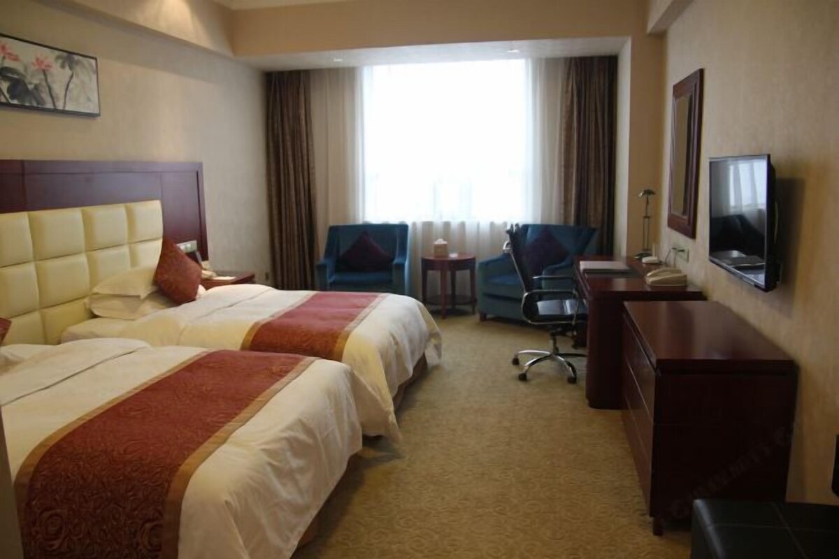 Une chambre d’hôtel avec deux lits, un bureau, une chaise, une télévision et une fenêtre avec des rideaux.