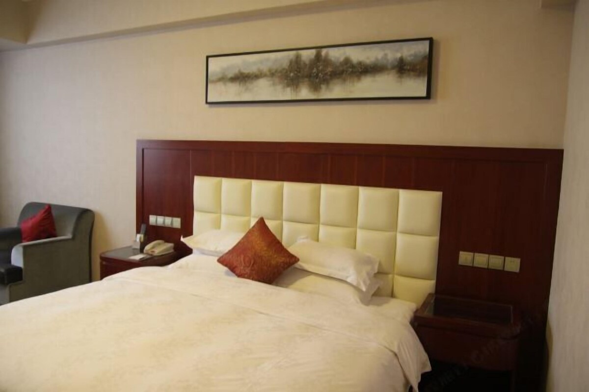 Une chambre d’hôtel avec un grand lit, une tête de lit, une table de chevet, une chaise et un tableau au mur.