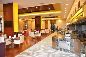 Un vestíbulo de hotel con una larga recepción, varias zonas de estar y una cocina moderna a la vista.
