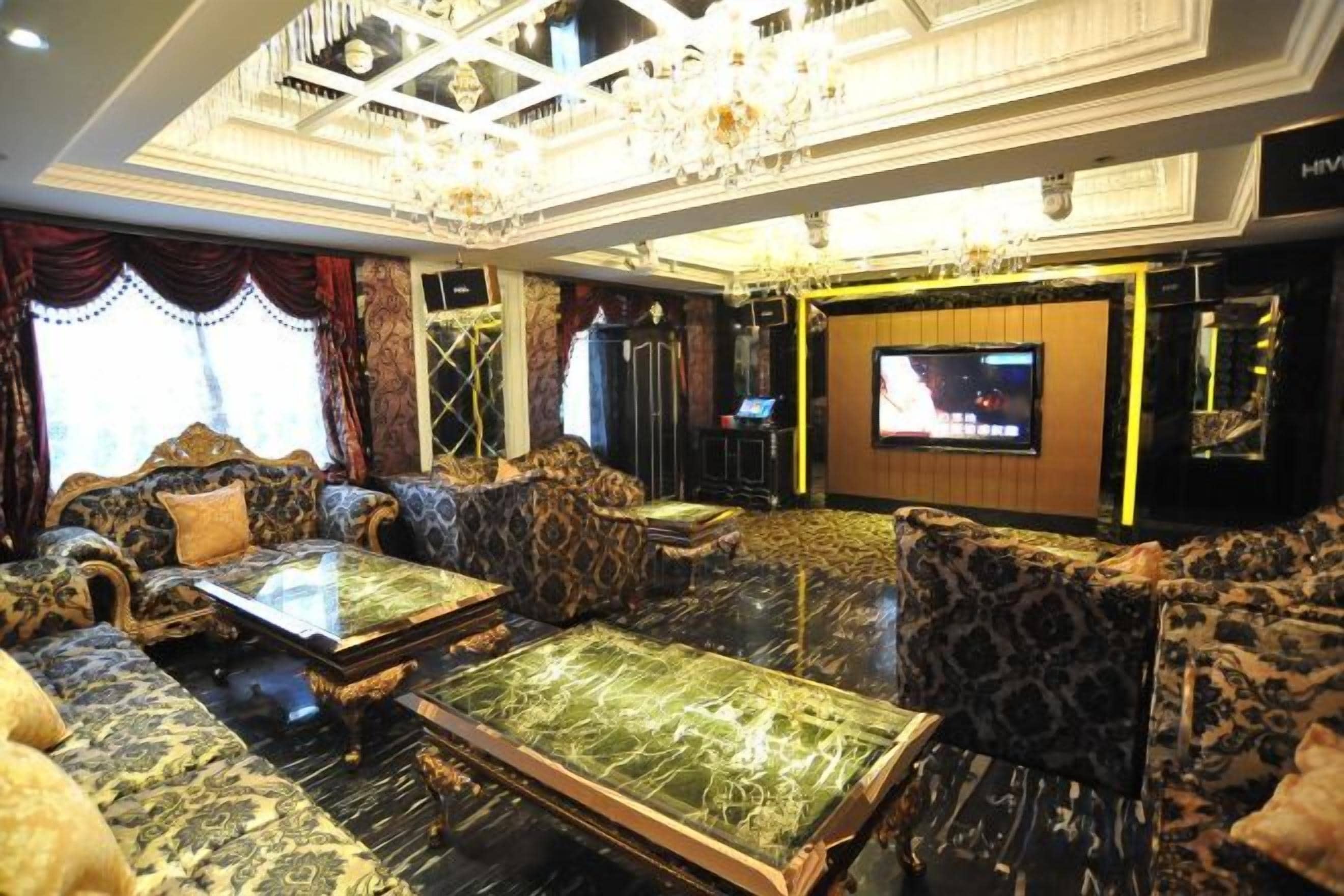 A luxurious hotel lobby with ornate furniture, a large flat-screen TV, and a chandelier.