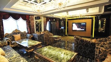 A luxurious hotel lobby with ornate furniture, a large flat-screen TV, and a chandelier.