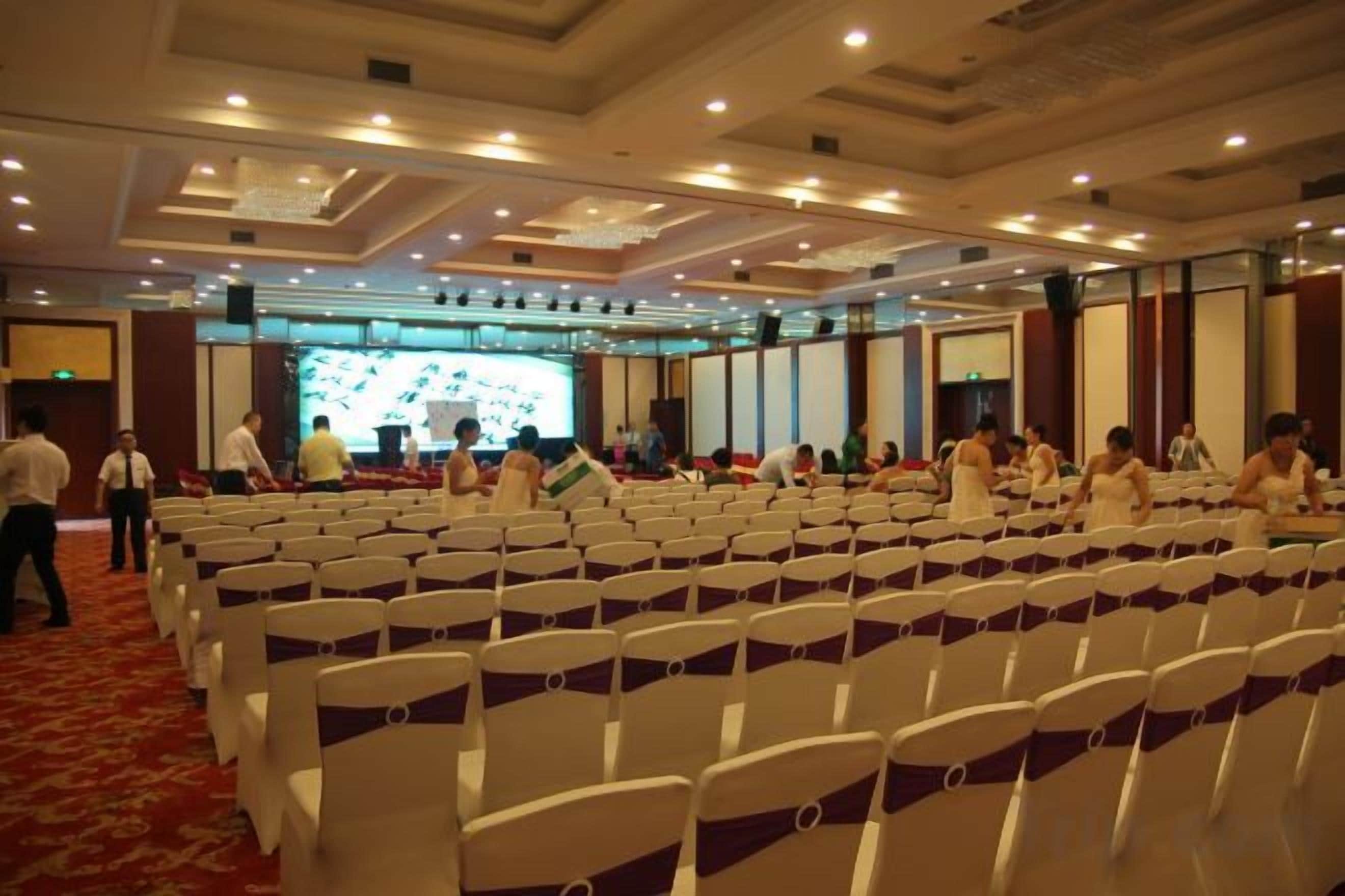 Un salón de conferencias con filas de sillas, un escenario y una pantalla grande.
