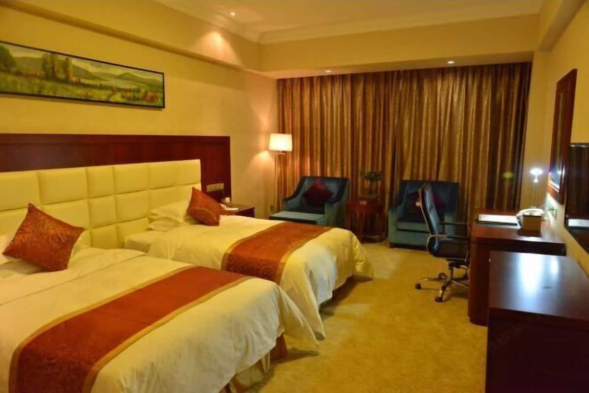 Une chambre d’hôtel avec deux lits, un bureau, une chaise, une lampe et un tableau au mur.