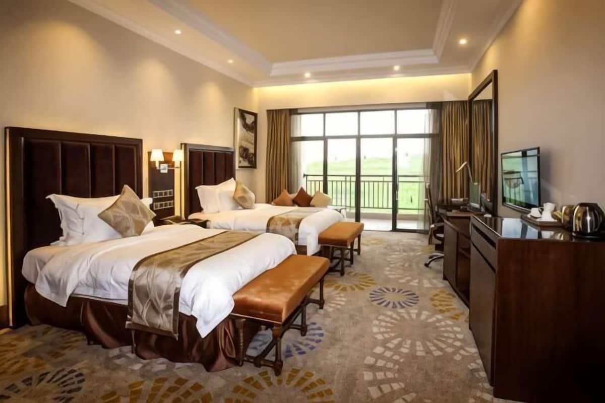 A hotel room with two beds, a desk, a TV, and a balcony with a view.