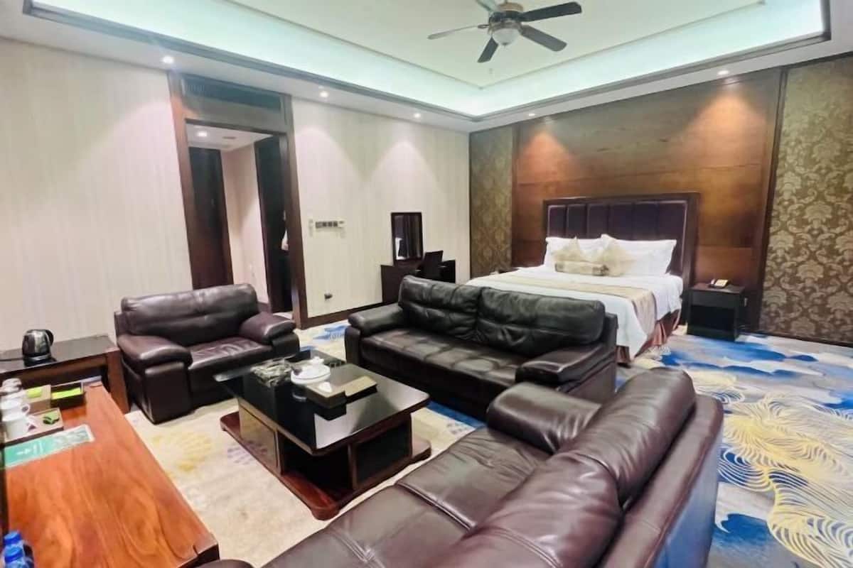 A hotel room with a bed, two leather sofas, a coffee table, a desk, and a ceiling fan.
