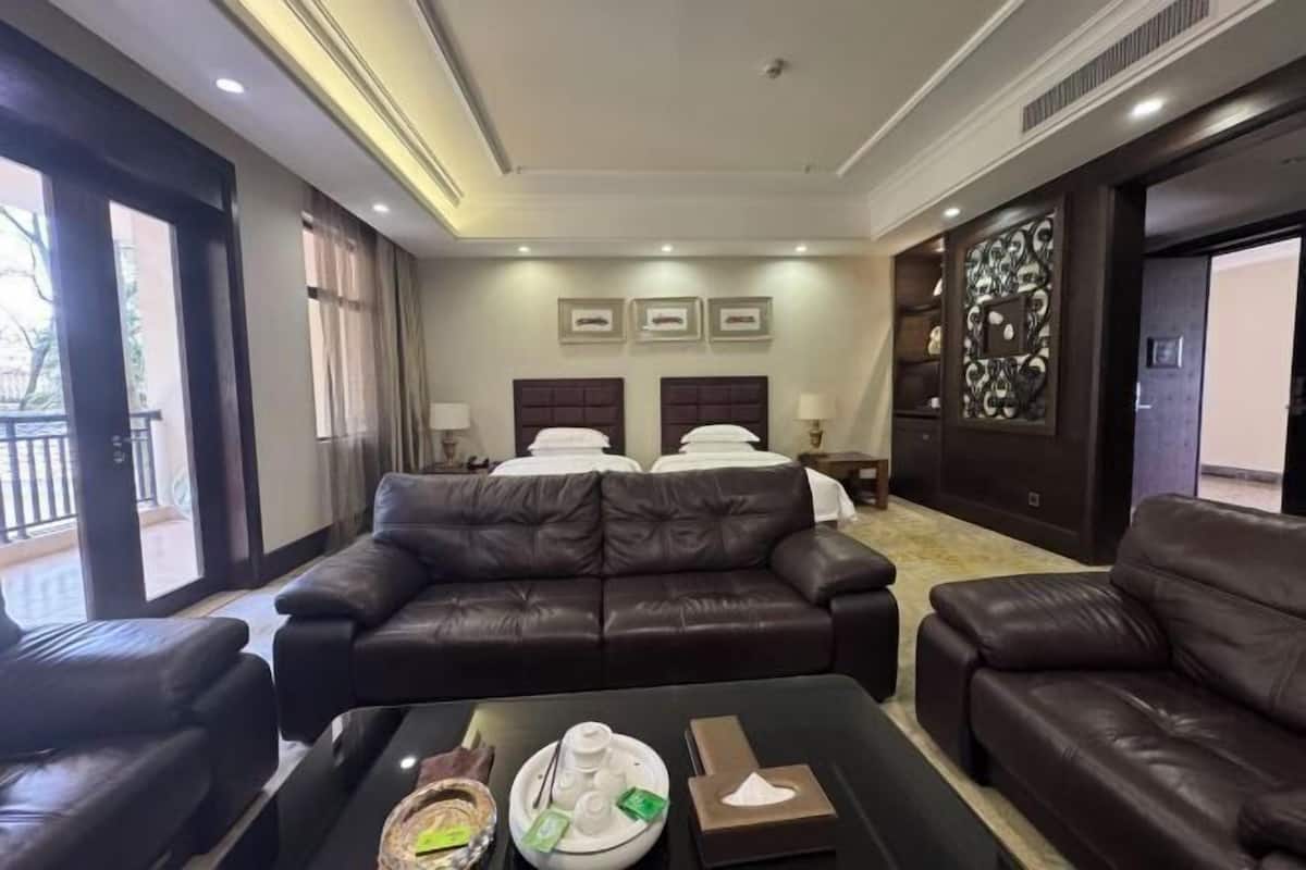 A hotel room with a leather sofa, a dining table with a tray, and a bed with white linens.