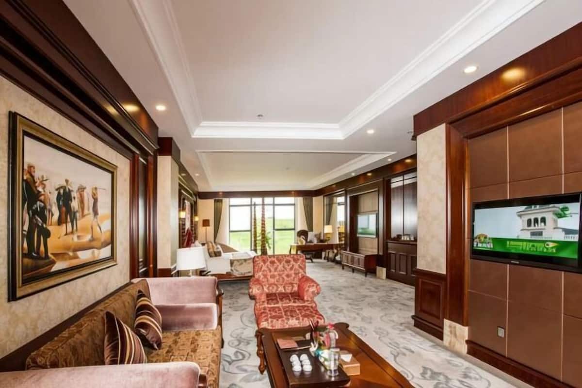 A hotel lobby with a sofa, armchairs, a coffee table, a television, and a painting on the wall.