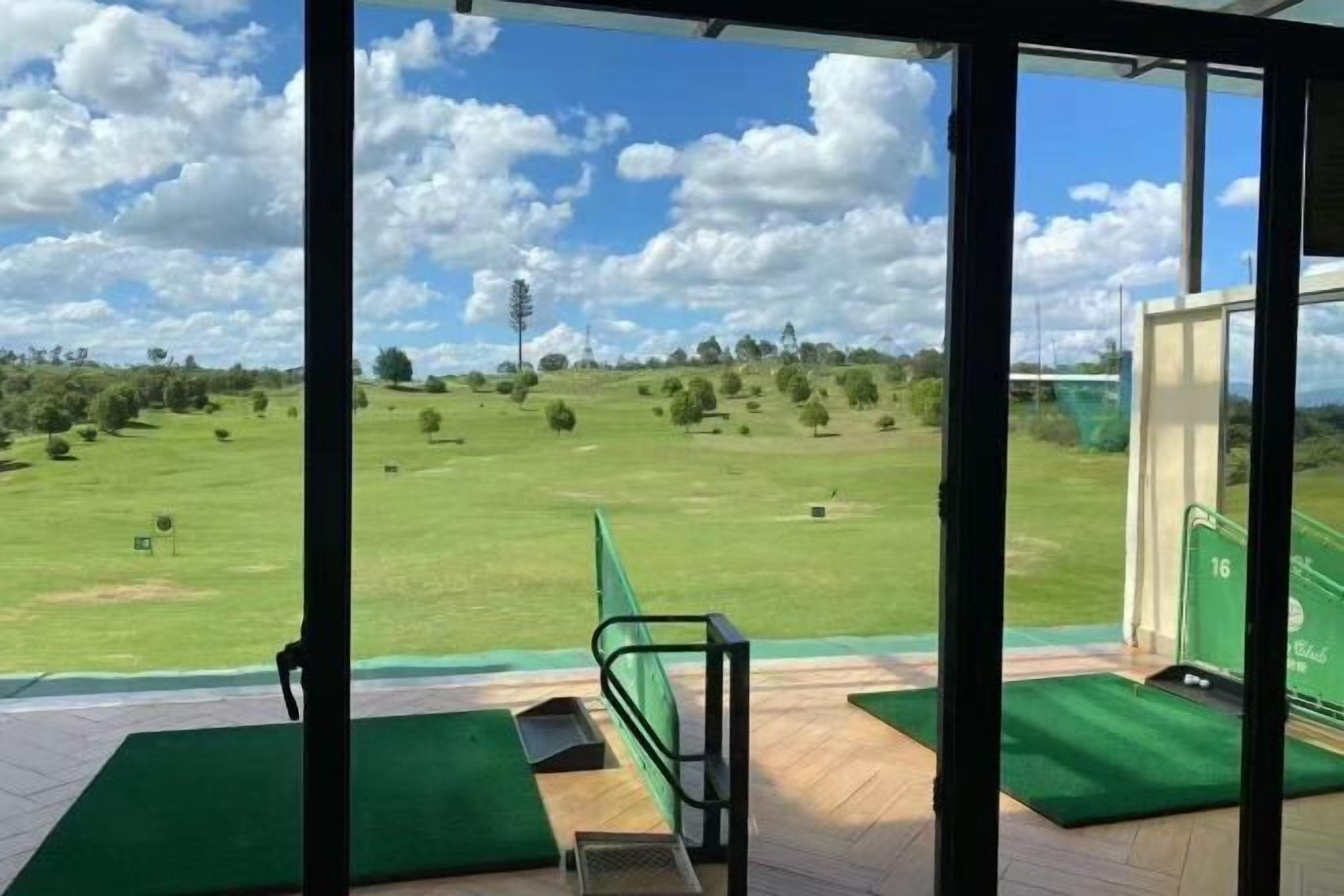 Vista de un campo de golf desde un espacio cubierto con un tapete verde y una barandilla de metal.