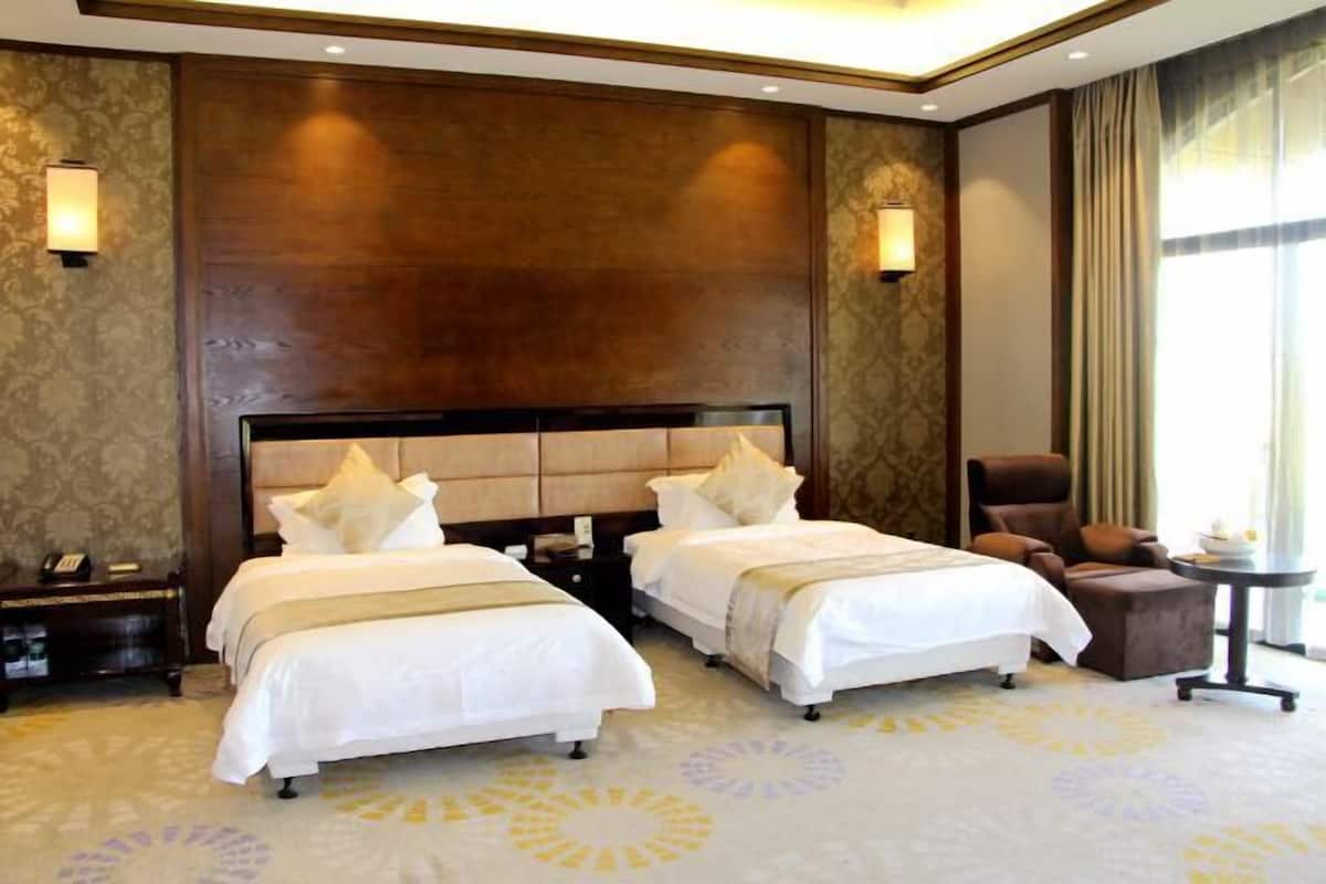 A hotel room with two beds, a brown headboard, a small table, a chair, and a nightstand with a phone.