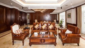 Un hall espacioso con un amplio sofá de cuero, sillones de madera y una mesa de centro. Se ve una escalera al fondo.
