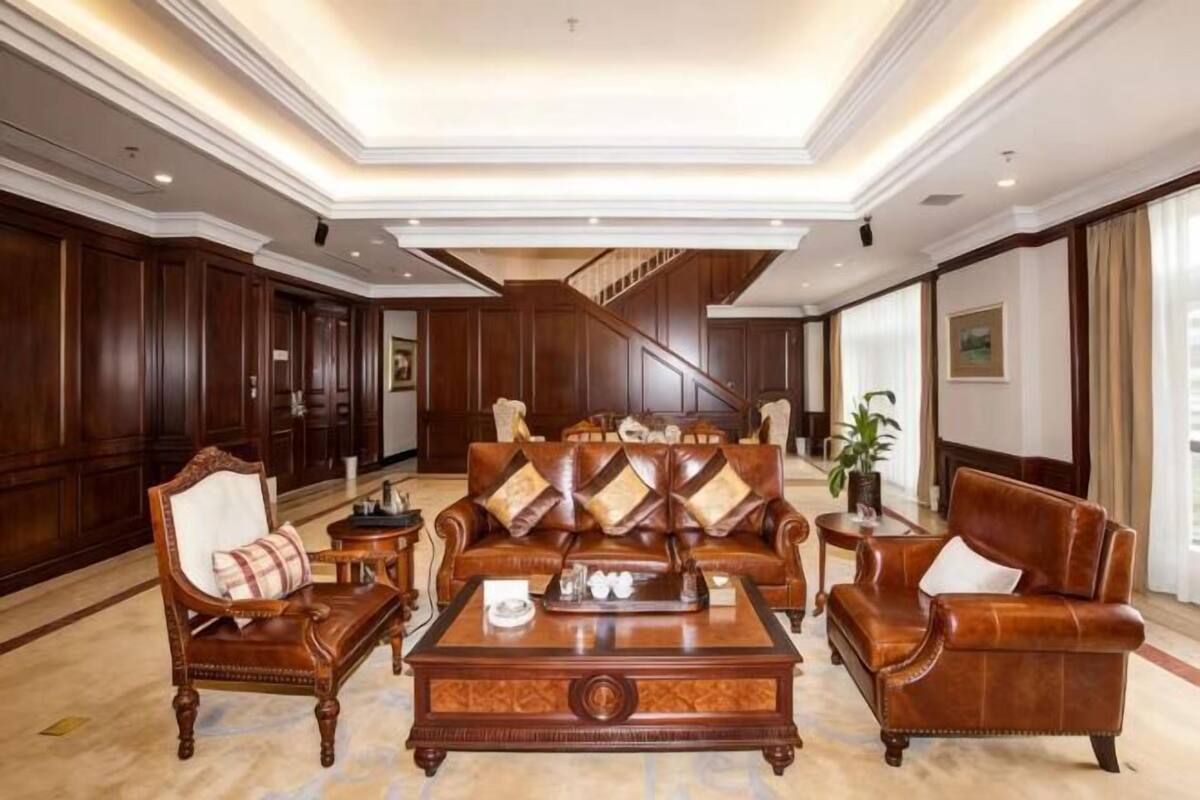 A spacious lobby with a large leather sofa, wooden armchairs, and a coffee table. A staircase is visible in the background.