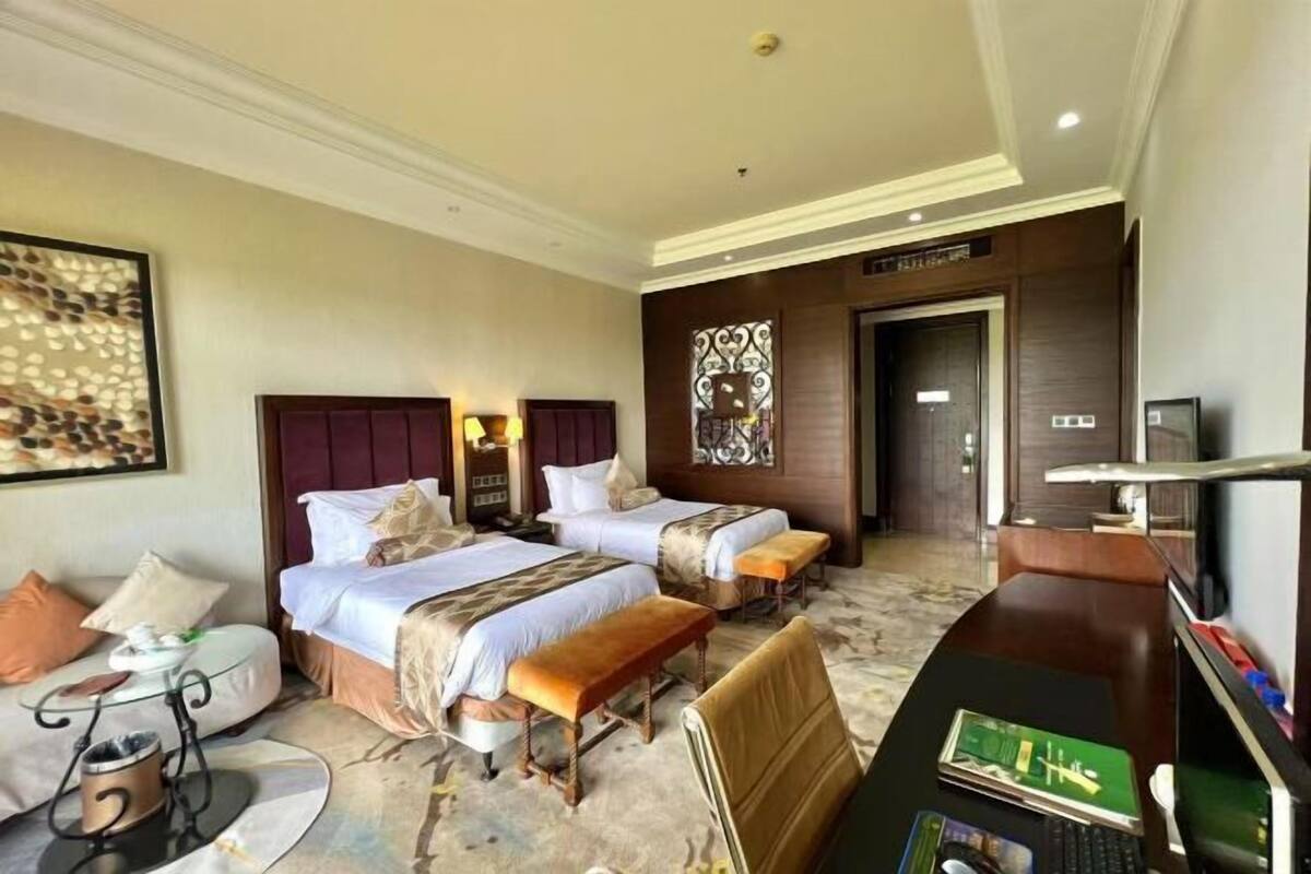 A hotel room with two beds, a desk with a computer, a chair, a coffee maker, and a decorative wall piece.