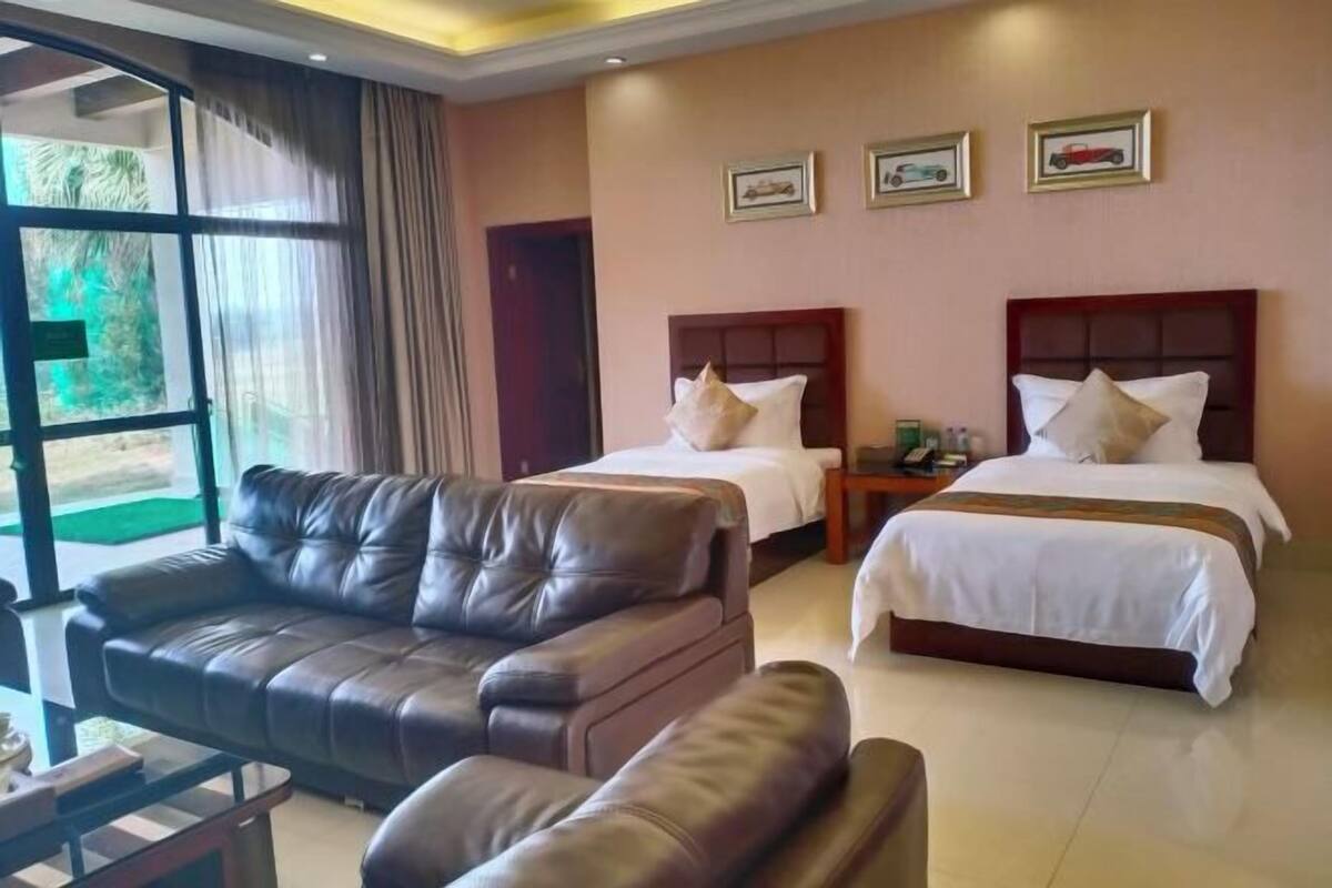 A hotel room with two beds, a leather sofa, a small table, and a window with curtains.