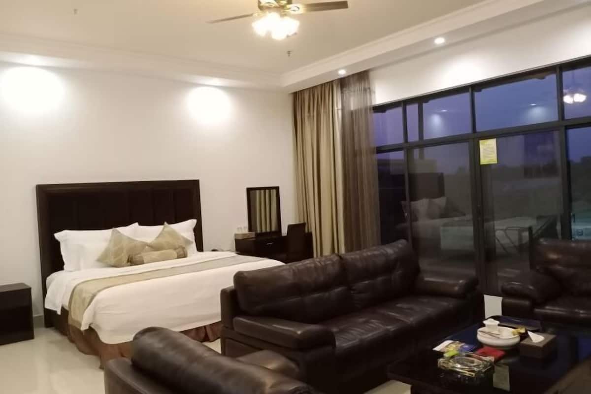 A modern hotel room with a large bed, leather sofa, and a glass coffee table.