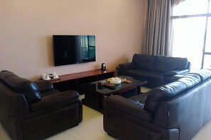 Una sala de estar con una televisión de pantalla plana, dos sofás, una mesa de centro y un ventanal con cortinas.