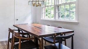Een eetruimte met een rechthoekige houten tafel en vier stoelen, een kroonluchter en een raam met uitzicht op groen.