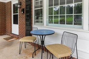Un patio con una mesa redonda y dos sillas, un muro de ladrillo, una ventana y una puerta.