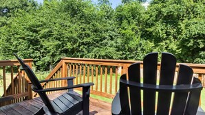 Een houten terras met twee Adirondack-stoelen gericht op een dicht, groen bos.
