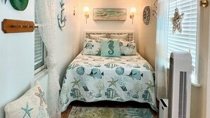 A bedroom with a bed, a chair, a heater, and wall decorations. - Cozy Cape Cottage (Brewster)