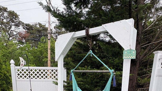 A garden with a hanging hammock, a wooden deck, and a white fence. - Cozy Cape Cottage (Brewster)
