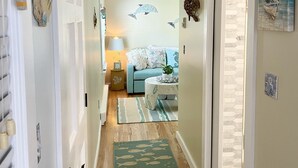 A hallway with a wooden floor, a green fish-patterned rug, a blue sofa, and a lamp. - Cozy Cape Cottage (Brewster)
