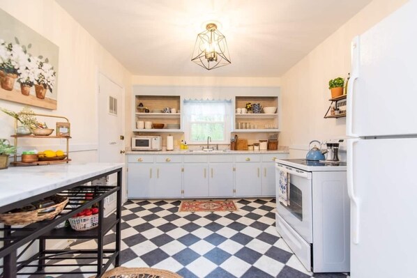 Una cocina con armarios blancos, suelo a cuadros blanco y negro, refrigerador blanco e lámpara colgante.