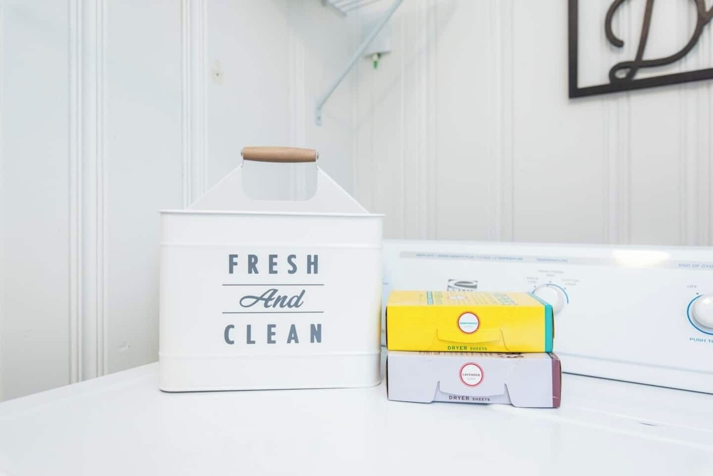 Een witte opslagcontainer met de tekst 'FRESH And CLEAN', een gele doos met de aanduiding 'DRYER SHEETS' en een witte droger.
