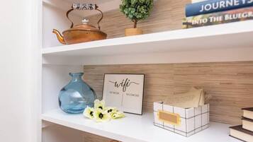 A bookshelf with a teapot, a small plant, a framed sign, a vase with flowers, and a stack of books.