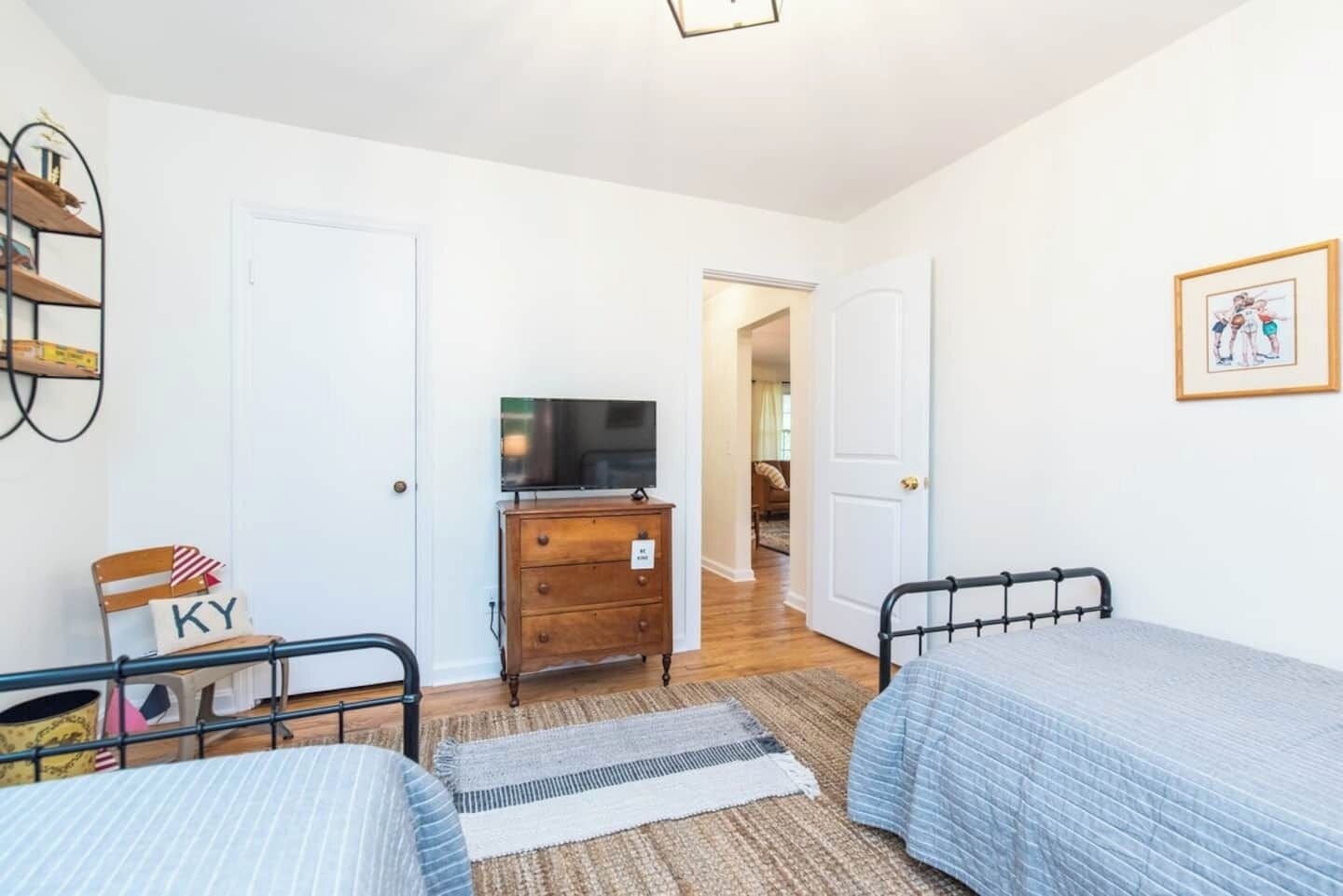Un dormitorio con dos camas, un aparador, un televisor y una puerta que da a otra habitación.