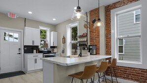 A modern kitchen with a central island, bar stools, and a brick accent wall. - Washington Guest House (Washington)
