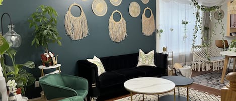 A living room with a dark green couch, a green armchair, a round coffee table, and a hanging macrame wall decoration.