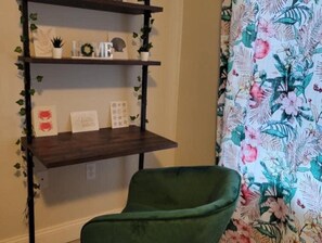 Ein Zimmer mit einem grünen Stuhl, einer Holzregal mit Dekorationen und einem blumigen Vorhang.