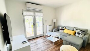 A modern living room with a grey sofa, a white coffee table, a white side table, and a television.