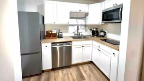 A compact kitchen with white cabinets, a stainless steel dishwasher, a microwave, and a sink.