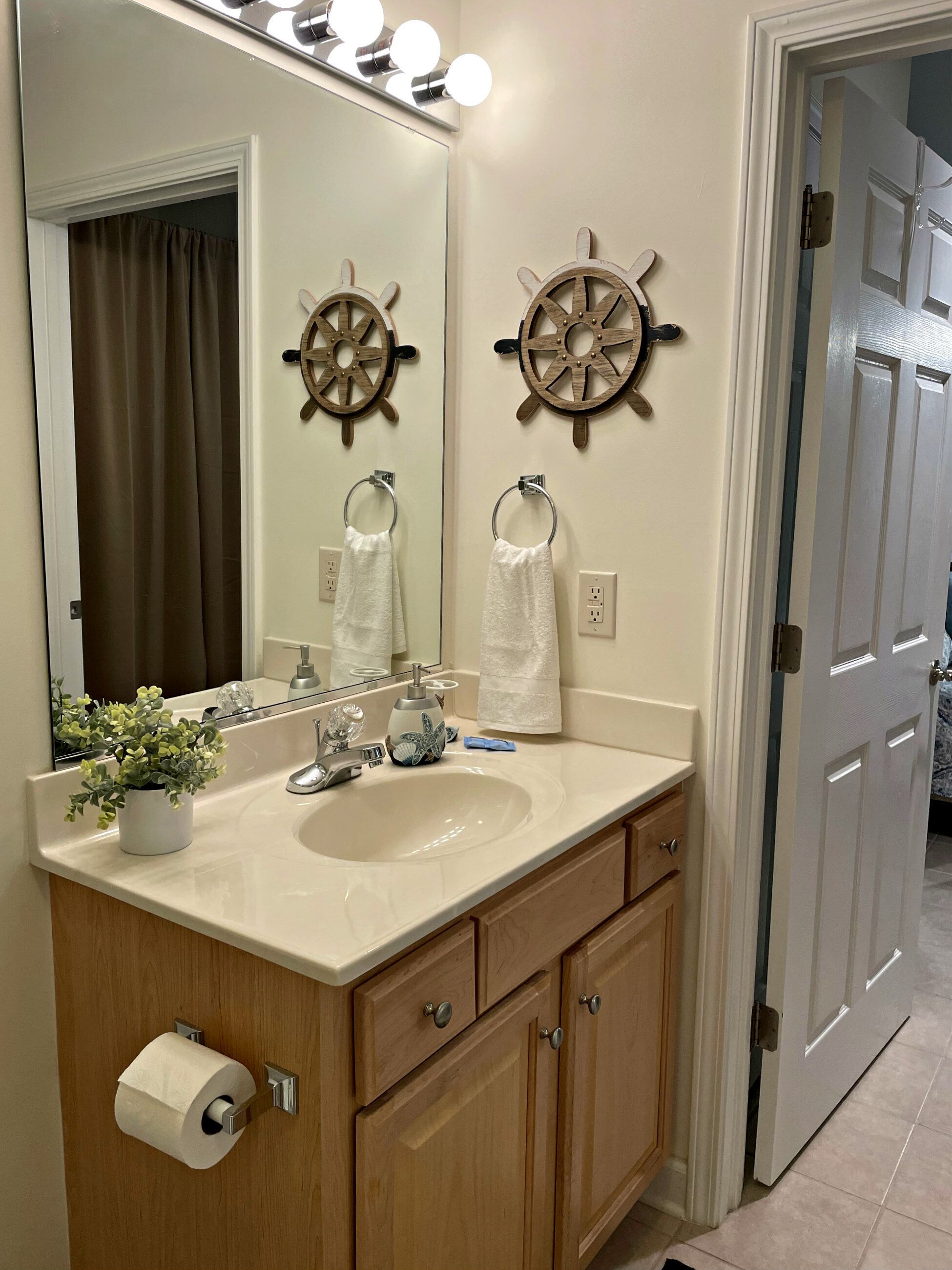 A bathroom with a sink, vanity, and two ship wheel decorations.