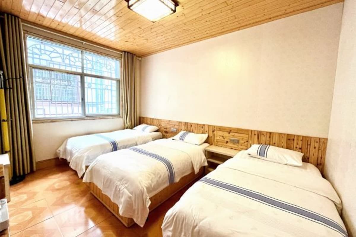 Quarto com duas camas, teto de madeira, janela grande com cortinas e piso de madeira.