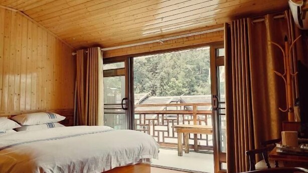 A wooden room with a bed, a table, and a view of the outdoors. - moranju hotel (Zhangjiajie)