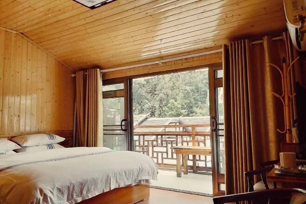 Ein Zimmer mit Holzboden, einem Bett, einem Tisch und Blick ins Freie.