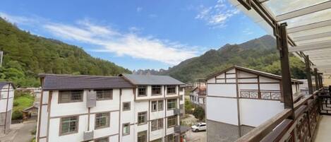 A residential building with multiple floors, a balcony, and a view of a mountainous landscape.